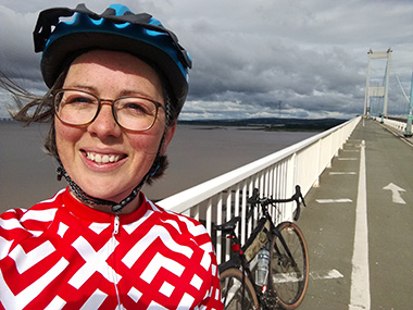 A woman standing on a bridge. There is a bicycle next to her