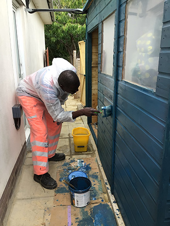 A man bending own painting a shed blue