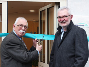 Two men standing outside a house cutting a ribbon